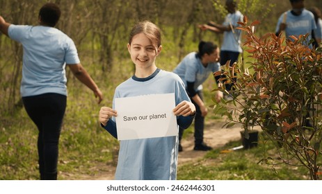 Portrait of sweet girl with save our planet poster against pollution and illegal dumping, volunteering to restore and preserve nature in the forest. Little child shows awareness sign. Camera A. - Powered by Shutterstock