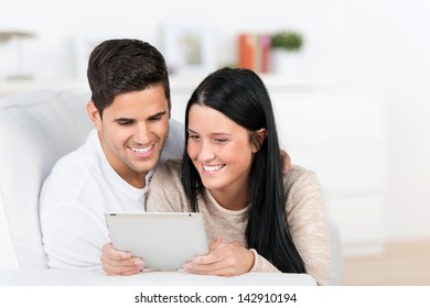 Portrait Of A Sweet Young Couple Using A Tablet Computer In Their Living Room And Smiling.