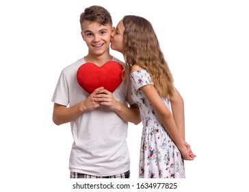 Portrait Of Sweet Young Teenagers Couple In Love - First Kiss. Teen Boy Holds Plush Heart In Hands. Teen Girl Kissing Teen Boy. Friendship And Love Concept.