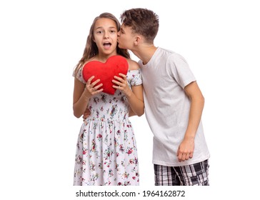 Portrait Of Sweet Young Teenagers Couple In Love - First Kiss. Teen Girl Holds Plush Heart In Hands. Teen Boy Kissing Teen Girl. Friendship And Love Concept