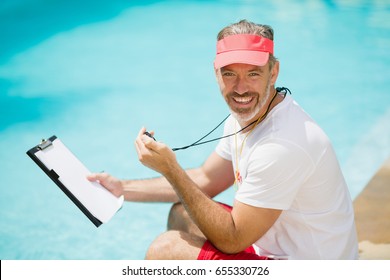 Portrait of swim coach holding stopwatch and clipboard near poolside on a sunny day - Powered by Shutterstock