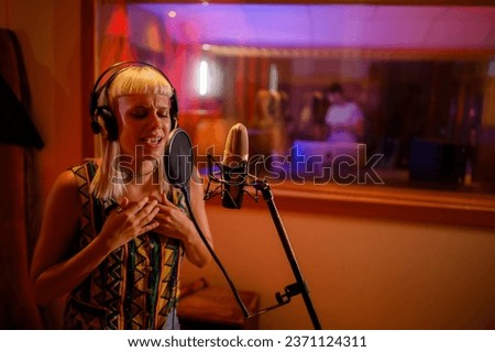 Portrait of a talented artist standing in a recording studio and singing a song during a recording session in a studio. A vocalist is singing and soloing in silent room booth in a music studio.