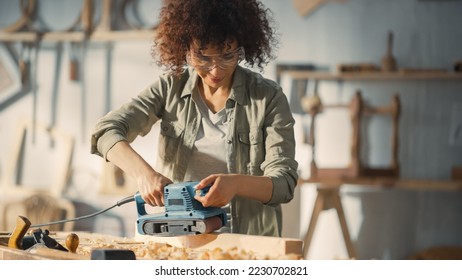 Portrait of a Talented Beautiful Artisan Carpenter Using Electric Sanding Machine to Polish a Wood Bar. Female Artist or Furniture Designer Working on a Project in a Loft Studio with Tools on Walls. - Powered by Shutterstock