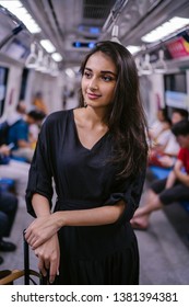 Portrait Of A Tall, Slim, Beautiful And Attractive Indian Asian Woman Riding The Train On Her Own With Her Luggage. She Is Heading To The City From The Airport. She Is Wearing A Casual Black Dress.