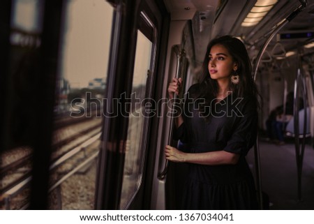 Portrait of a tall, slim, elegant and beautiful Indian Asian woman taking the train alone. She is leaning near the window and watching the scenery go by. The train is modern and clean.