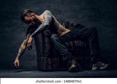 Portrait of tattooed sad man in despair, which is sitting on armchair at dark stash. - Shutterstock ID 1488487961