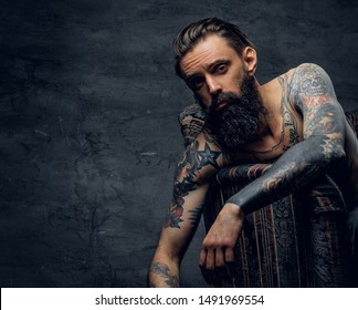 Portrait of tattooed sad man in despair, which is sitting on armchair at dark stash. - Shutterstock ID 1491969554