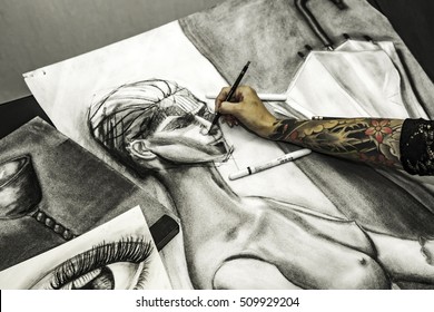 Portrait tattooed woman artist showing her charcoal drawing in studio. High angle