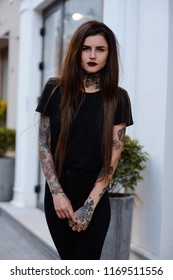 Portrait of tattooed young female model in black. Beautiful slim girl with black lips tattoos and piercing wearing casual  black clothes outside. Alternative lifestyle