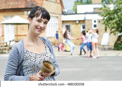 Portrait Of Teacher With Bell Supervising Break In School Playground