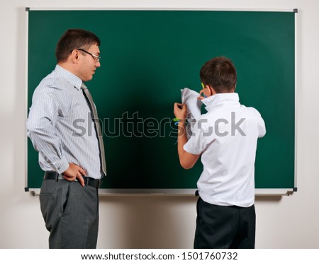 Portrait of a teacher and funny schoolboy with low discipline. Pupil very emotional, having fun and very happy, posing at blackboard background - back to school and education concept