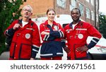 Portrait of team of paramedics in red medical uniform posing outdoors. Male and female doctors standing in street near ambulance and smiling at camera. Medical workers. Professional nurses, first aid