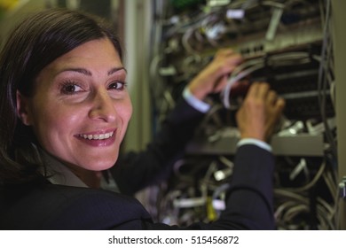 Portrait of technician checking cables in a rack mounted server in server room