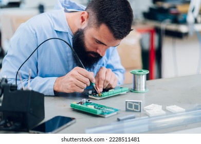 Portrait of a technician repairs circuit board of a device with iron soldering and tin wire. Concentrated while working. Electronics engineer repairing a device in his workshop. Copy space. - Powered by Shutterstock