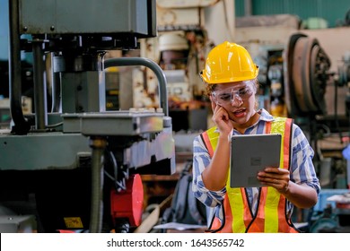 Portrait Of Technician Or Worker Woman With Engineer Uniform Yellow Helmet And Hold Tablet Check Or Maintenance The Machine In Factory Workplace. She Also Action Of Serious Thinking For Good Industry.