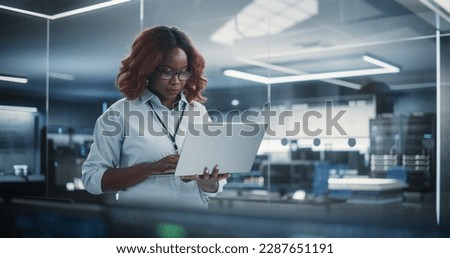 Portrait of a Technological Software Engineering Department Manager Standing and Using a Laptop Computer. African Female Looking in the Distance and Thinking while Working in the Office