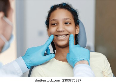 Portrait of teen black girl with toothy smile sitting in a dental chair at dentistry clinic - Powered by Shutterstock