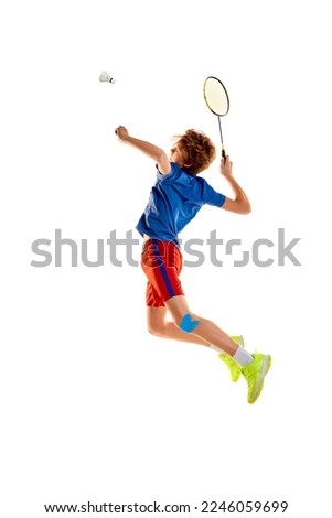 Portrait of teen boy in uniform playing badminton, serving shuttlecock with racket in a jump isolated over white background. Concept of sportive lifestyle, motion, action, competition