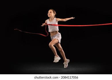 Portrait Of Teen Girl Crossing Red Ribbon Isolated Over Black Background. Running Athlete. Concept Of Action, Sport, Healthy Life, Competition, Motion, Physical Activity. Copy Space For Ad