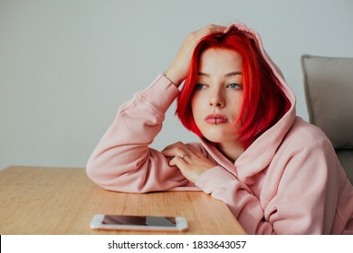Portrait of a  teen girl holding head on desk waiting for text message on cell phone device looking at window