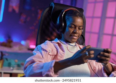 Portrait of teenage African American girl playing mobile games while relaxing at home at night - Powered by Shutterstock