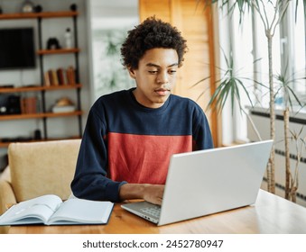 Portrait of teenage black boy using laptop computer at home. Teenage boy attending to online school class - Powered by Shutterstock