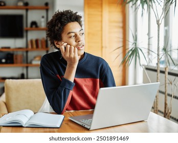 Portrait of teenage black boy using laptop computer and thinking and day dreaming looking through window at home. Teenage boy attending to online school class - Powered by Shutterstock