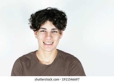 Portrait of a teenage boy with a beautiful smile on a light background. The boy has long curly dark hair and healthy teeth after wearing braces. Dental concept