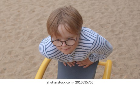 Portrait of a teenage boy in a children's park. Glasses improve vision and perception of the world. Sand underfoot. Waiting to meet a friend.
