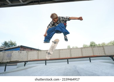 Portrait Of Teenage Boy Doing Skateboard Tricks In Air At Outdoor Skatepark In Urban Area