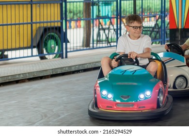 Portrait of teenage boy in glasses driving an electric car in amusement park. Child on Bumper car