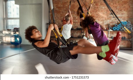 Portrait Of Teenage Boy Having Fun While Training Using Fitness Straps In Gym With Other Kids. Sport, Healthy Lifestyle, Physical Education Concept. Horizontal Shot