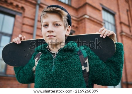 Portrait of teenage boy holding skateboard looking at camera while standing outdoors in the city