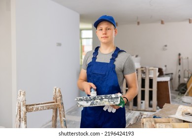 Portrait Of Teenage Boy Wearing Coverall Standing At Stepladder In Building Site. Young Man With Paint Roller Working On Part-time Job As Painter.