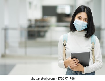 Portrait of a teenage college student wears medical face mask with school backpack to protect from influenza virus, COVID-19 pandemic in college building. Back to school. Education stock photo