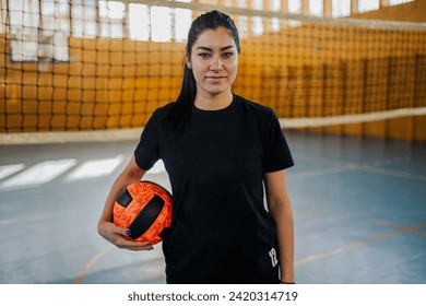 Portrait of a teenage female professional volleyball player standing on volleyball court with ball and smiling at the camera during training. A happy young sportswoman in shape posing with volleyball. - Powered by Shutterstock
