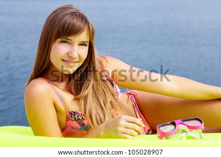 Portrait of teenage girl in bikini lying on mattress and looking at camera
