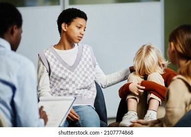 Portrait of teenage girl comforting little boy crying in group therapy session with diverse children