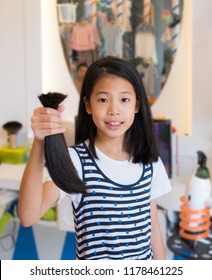 Portrait Of Teenage Girl Donating Her Healthy Hair To Cancer Patient Who Lost Hair. Asian Kid Holding, Showing Her Ponytail After Haircut, Generously Donating Long Hair For Making Wig In Beauty Salon.