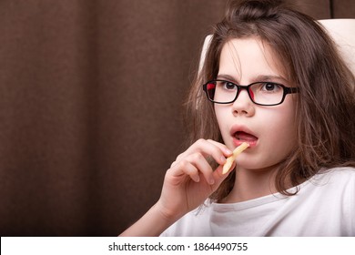 Portrait Of A Teenage Girl With Glasses Holding French Fries With Her Mouth Open, Very Surprised, Puzzled, Alarmed In The Dark Background. Concept Of Emotional Food Addiction, Binge-eating Disorder.