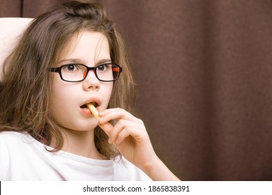 Portrait Of A Teenage Girl With Glasses Holding French Fries With Her Mouth Open, Very Surprised, Puzzled, Alarmed In The Dark Background. Concept Of Emotional Food Addiction, Binge-eating Disorder.