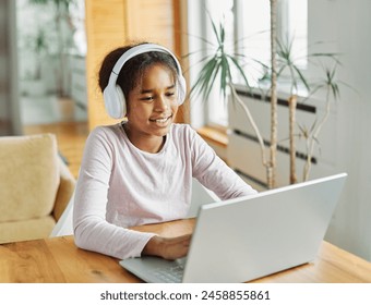 Portrait of a teenage girl having fun using laptop wearing headphones and listening to the sound or doing homework and learning with laptop at home - Powered by Shutterstock