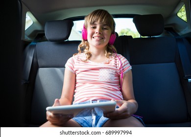 Portrait of teenage girl in headphones using digital tablet in the back seat of car - Powered by Shutterstock