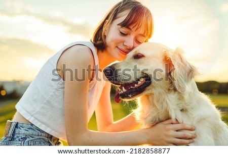 A Portrait of teenage girl petting golden retriever outside in sunset