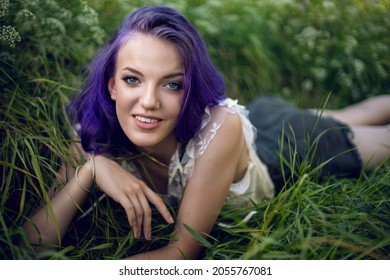 Portrait Of A Teenage Girl With Purple Hair And An Earring In Her Nose Lying In The Grass In Nature