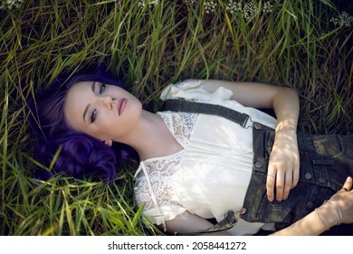 Portrait Of A Teenage Girl With Purple Hair And An Earring In Her Nose Lying In The Grass In Nature