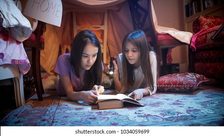 Portrait of teenage girls reading book in bedroom at night
