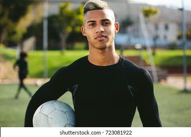 Portrait of teenage soccer player holding a football in his hand and looking at camera. Young man during training on football field.