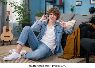 Portrait Of Teenager Boy Dressed In Jeans Pants And Shirt Is Hanging Out In The Living Room At Home. The Boy Is Listening A Concert Of His Favorite Band On Headphones Looking At Camera.