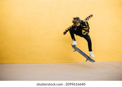 Portrait Of Teenager Boy Jumping With An Skateboard In Front Of A Yellow Wall On His Way To School